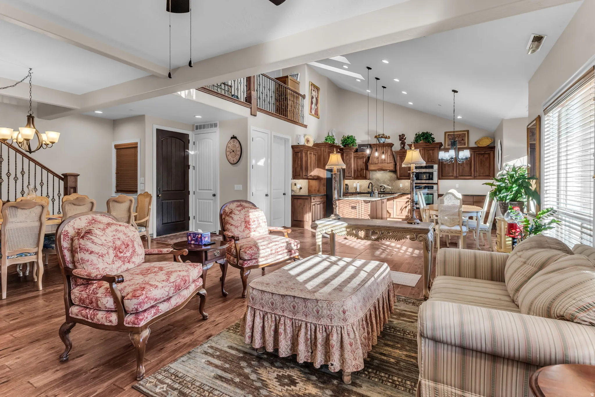 Vaulted ceiling with exposed beams, wood-finish flooring, staircase with wrought iron railing, kitchen island with built-in sink, and custom wood cabinetry