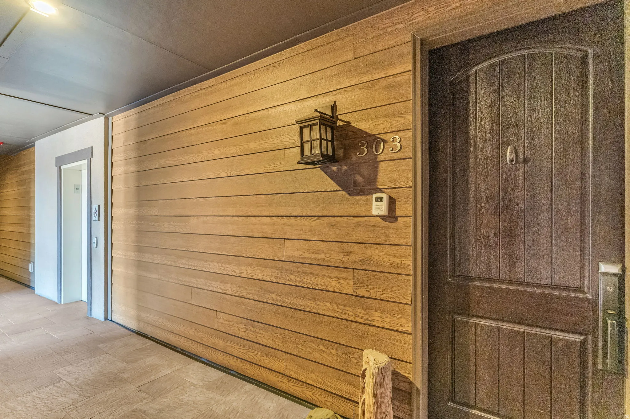 Textured wood-finish wall paneling, arched entry door, and wall-mounted exterior lighting fixture elevator access