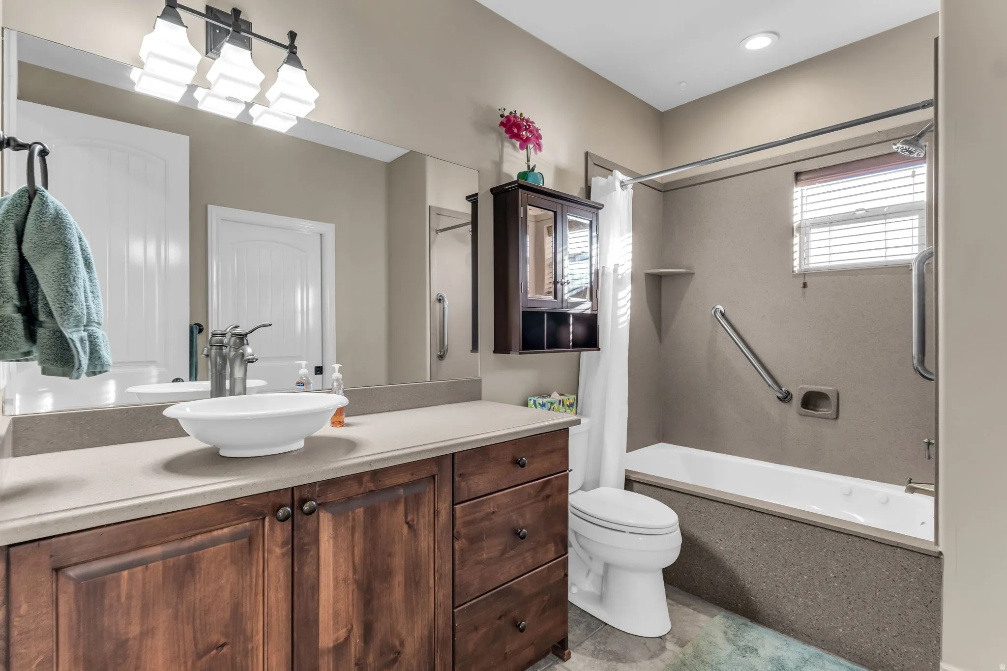 Wood-finish vanity with a vessel sink, full-width mirror, bath area with grab bars for easy out access.