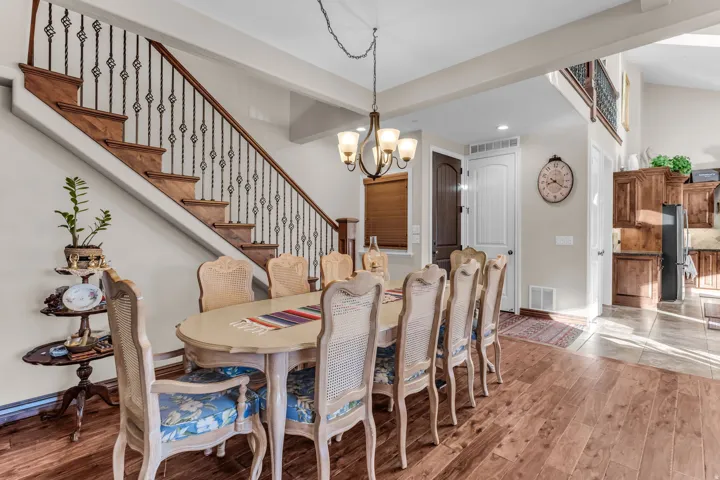 Hardwood flooring, wood staircase with ornate iron balusters, vaulted ceiling, and a multi-light chandelier