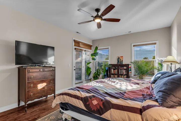 Warm wood-finish flooring, a ceiling fan with integrated lighting, and multiple windows with blinds