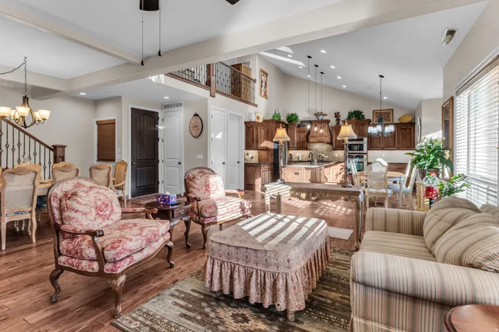 Vaulted ceiling with exposed beams, wood-finish flooring, staircase with wrought iron railing, kitchen island with built-in sink, and custom wood cabinetry