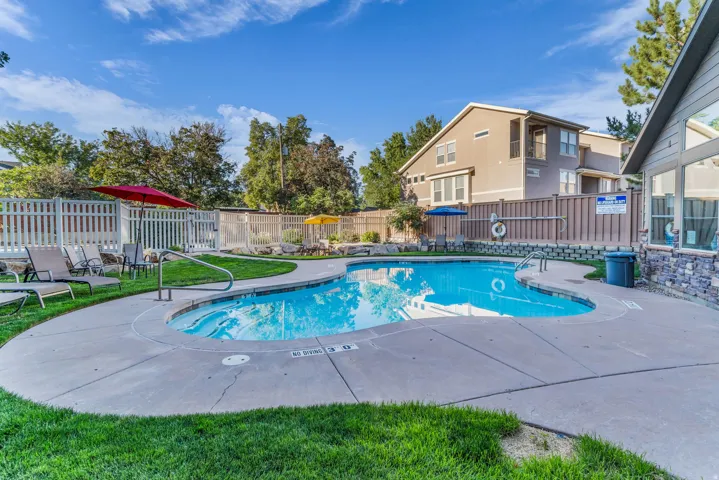 Outdoor pool with concrete decking, surrounding green space, and a white picket fence