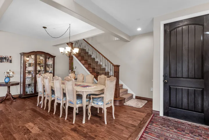 Wood-finish flooring, staircase with wrought iron balusters, recessed lighting, and a dark wood-paneled entry door