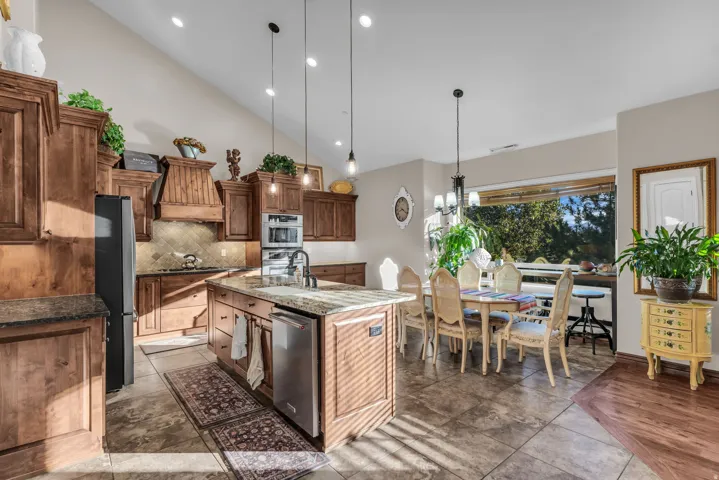 Vaulted ceiling with recessed lighting, wood cabinetry, stone countertops, and a kitchen island with an integrated sink and dishwasher