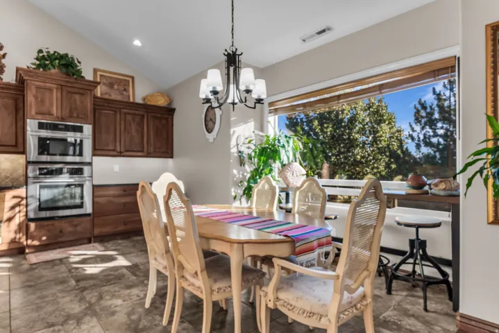 Vaulted ceiling, dark wood cabinetry, built-in stainless steel double oven, large picture window with wood blinds, and tile flooring