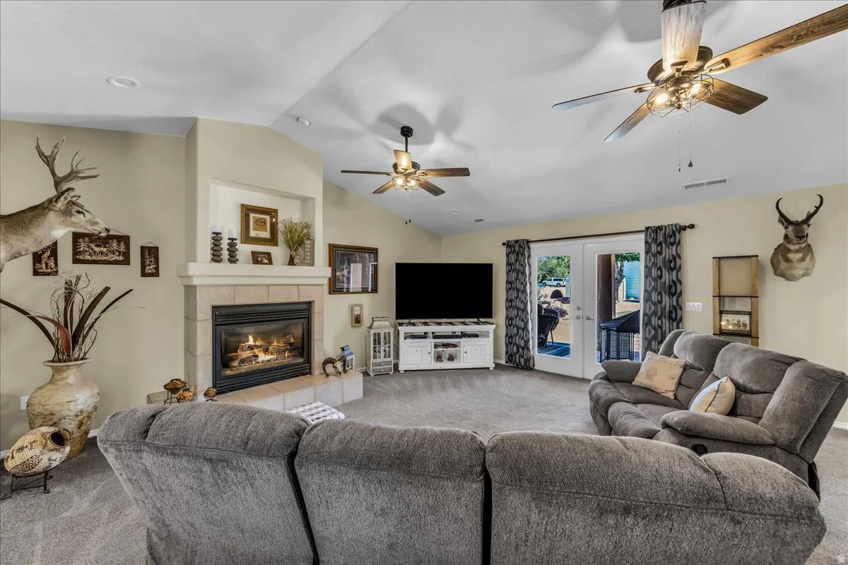 Carpeted living area featuring a stone-clad fireplace with mantel, recessed lighting, and multiple ceiling fans