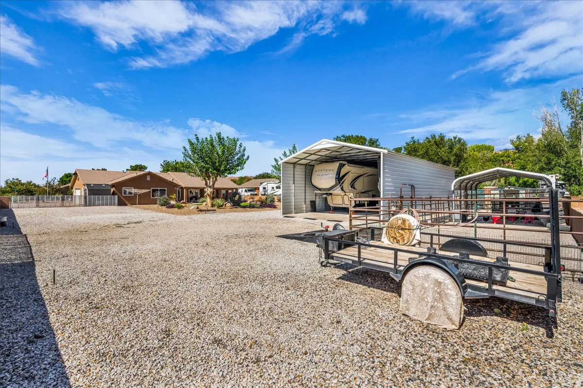 Gravel lot with a large metal carport, second metal structure, and a single-story residence in the background