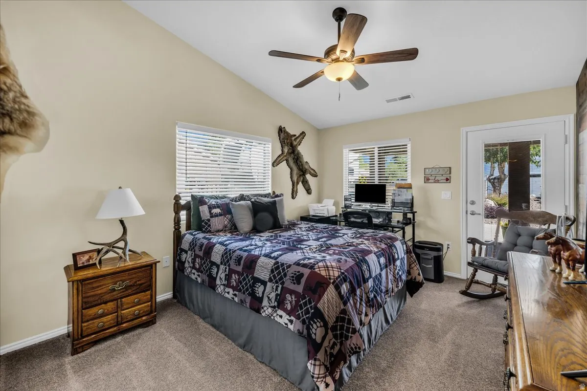 Vaulted ceiling with a ceiling fan, carpet flooring, two windows with blinds, and a glass-paneled exterior door