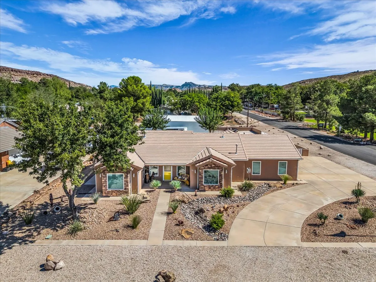 Brick ranch-style residence featuring a metal composition roof, arched entryway, and professional landscaping with mature trees and desert-adapted plantings