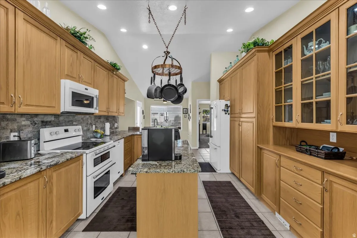 Kitchen featuring wood cabinetry, granite countertops, tile flooring, and integrated white appliances