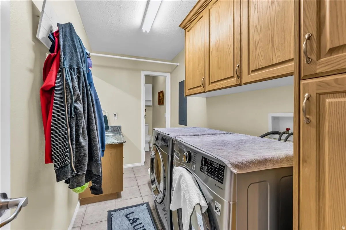 Laundry area featuring wood cabinetry, tiled flooring, and a built-in utility sink with a stone-finish countertop