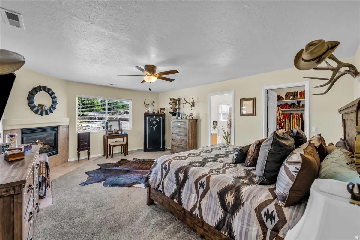 Carpeted bedroom with a built-in fireplace, a ceiling fan, a window with blinds, and a walk-in closet