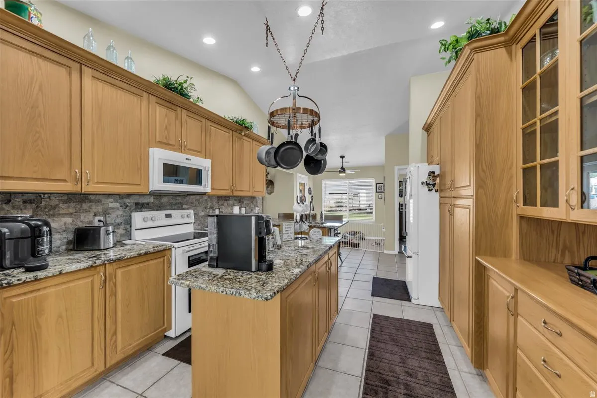 Kitchen featuring wood-finish cabinetry, granite countertops, tile flooring, a stone-look backsplash, and recessed lighting