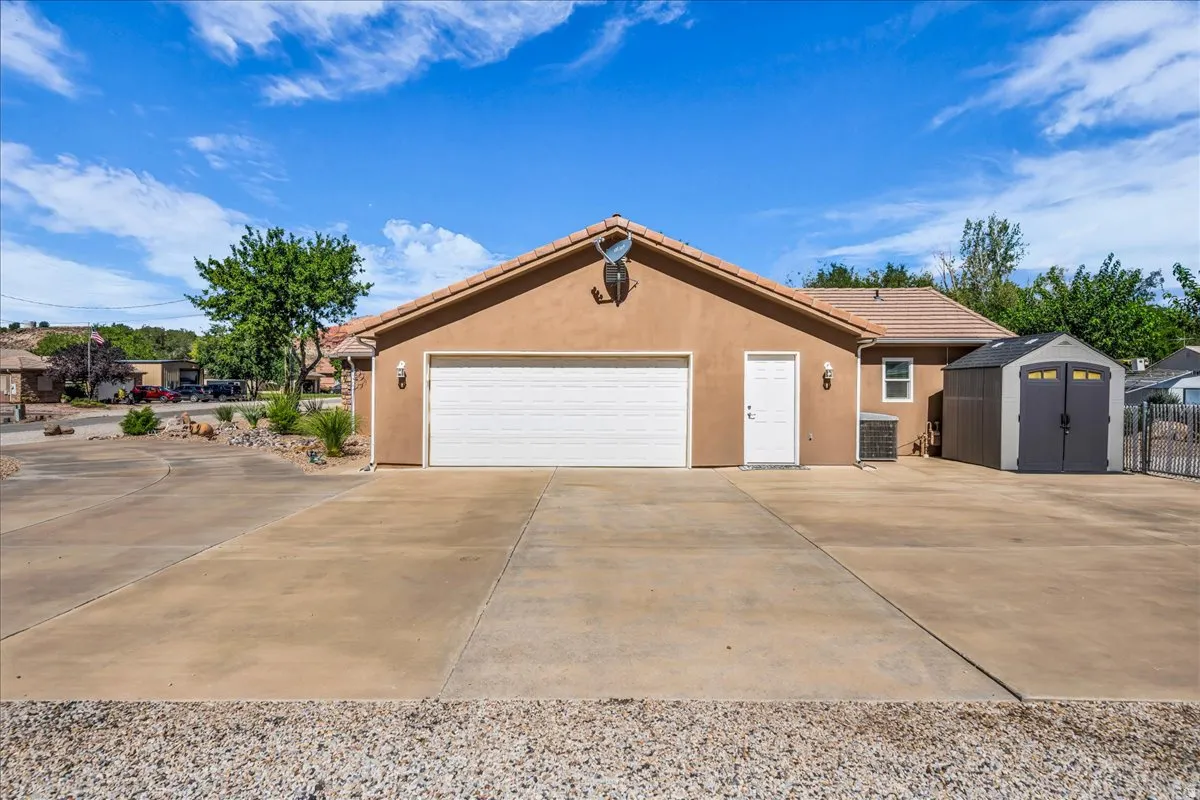 Stucco exterior with a two-car garage, concrete driveway, and an outdoor storage shed