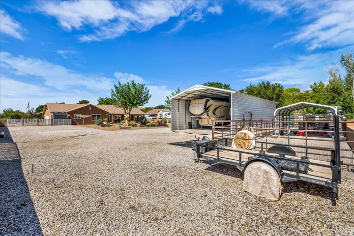 Gravel lot with a large metal carport, second metal structure, and a single-story residence in the background