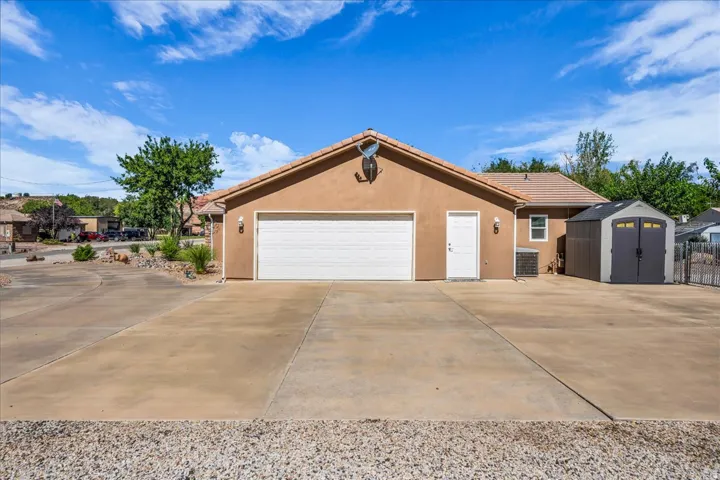 Stucco exterior with a two-car garage, concrete driveway, and an outdoor storage shed