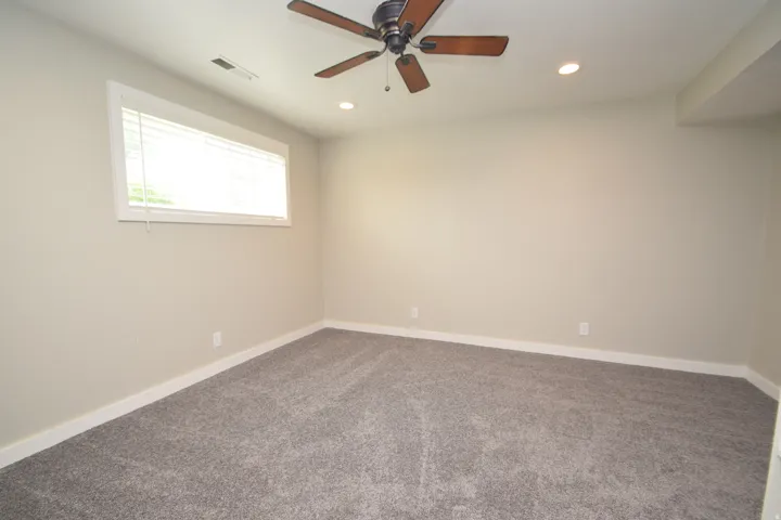 Recessed lighting, ceiling fan with wood-finish blades, and neutral-toned carpeting