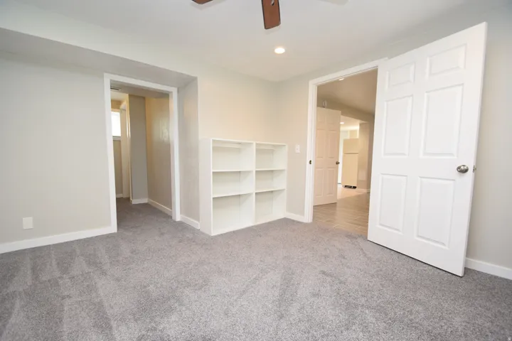 Plush gray carpeting, recessed ceiling lighting, built-in shelving, white paneled doors, and a ceiling fan