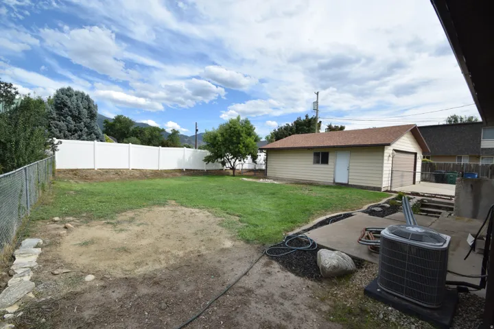 Expansive backyard featuring a partial white vinyl privacy fence, chain link fencing, a detached garage with a single bay door, and a concrete patio