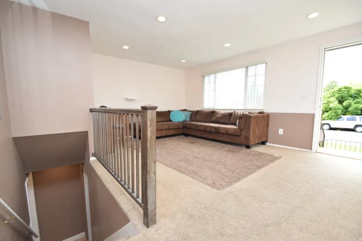 Recessed lighting, large window, carpet flooring, staircase with wood railing, glass panel door
