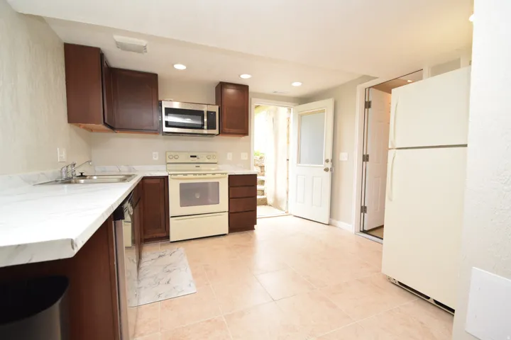 Kitchen featuring wood-finish cabinetry, light-toned countertops, recessed lighting, and tile flooring