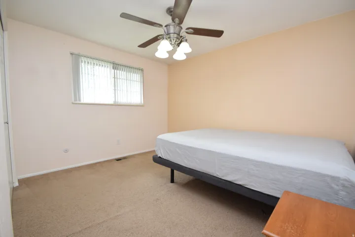 Wall-to-wall carpeting, ceiling fan with light kit, and a window with horizontal blinds