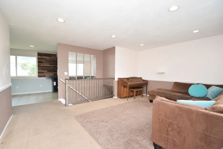 Recessed lighting illuminates the carpeted living area with a partial wall and railing separating spaces