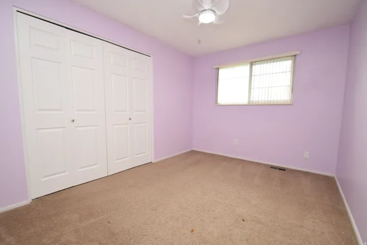 Built-in closet with four-panel bi-fold doors, overhead ceiling fan, and window with horizontal blinds