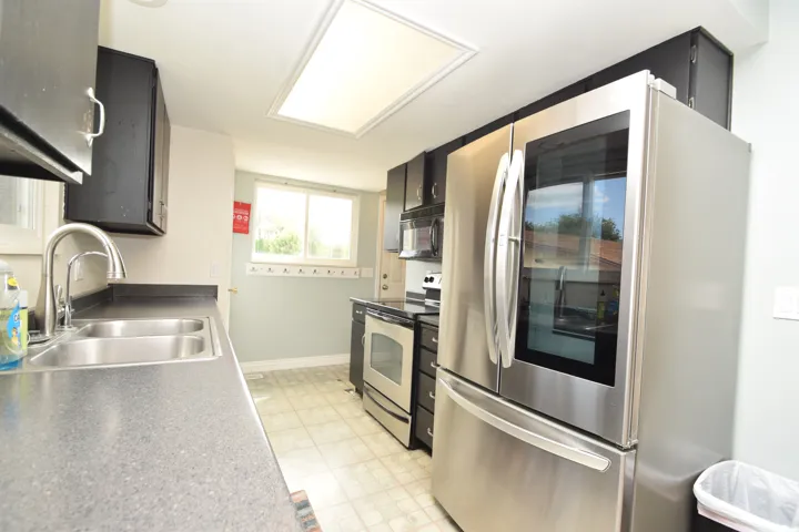 Kitchen featuring stainless steel appliances, dark cabinetry, a dual basin sink, and a skylight