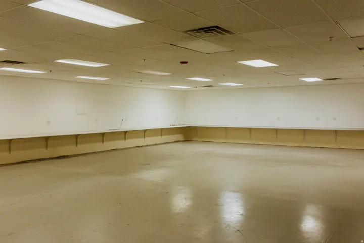 Expansive open space with light-colored flooring, extensive built-in shelving, white walls, and a suspended acoustic tile ceiling with integrated lighting