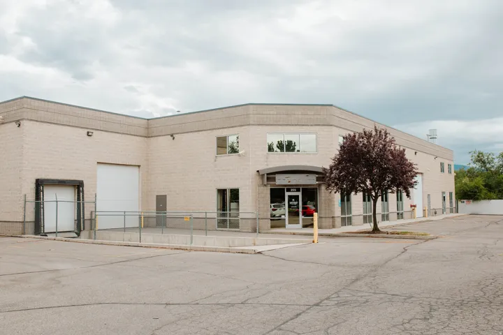 Commercial building featuring a light-colored brick exterior, multiple large windows, a prominent main entrance, a loading dock, and a large roll-up door