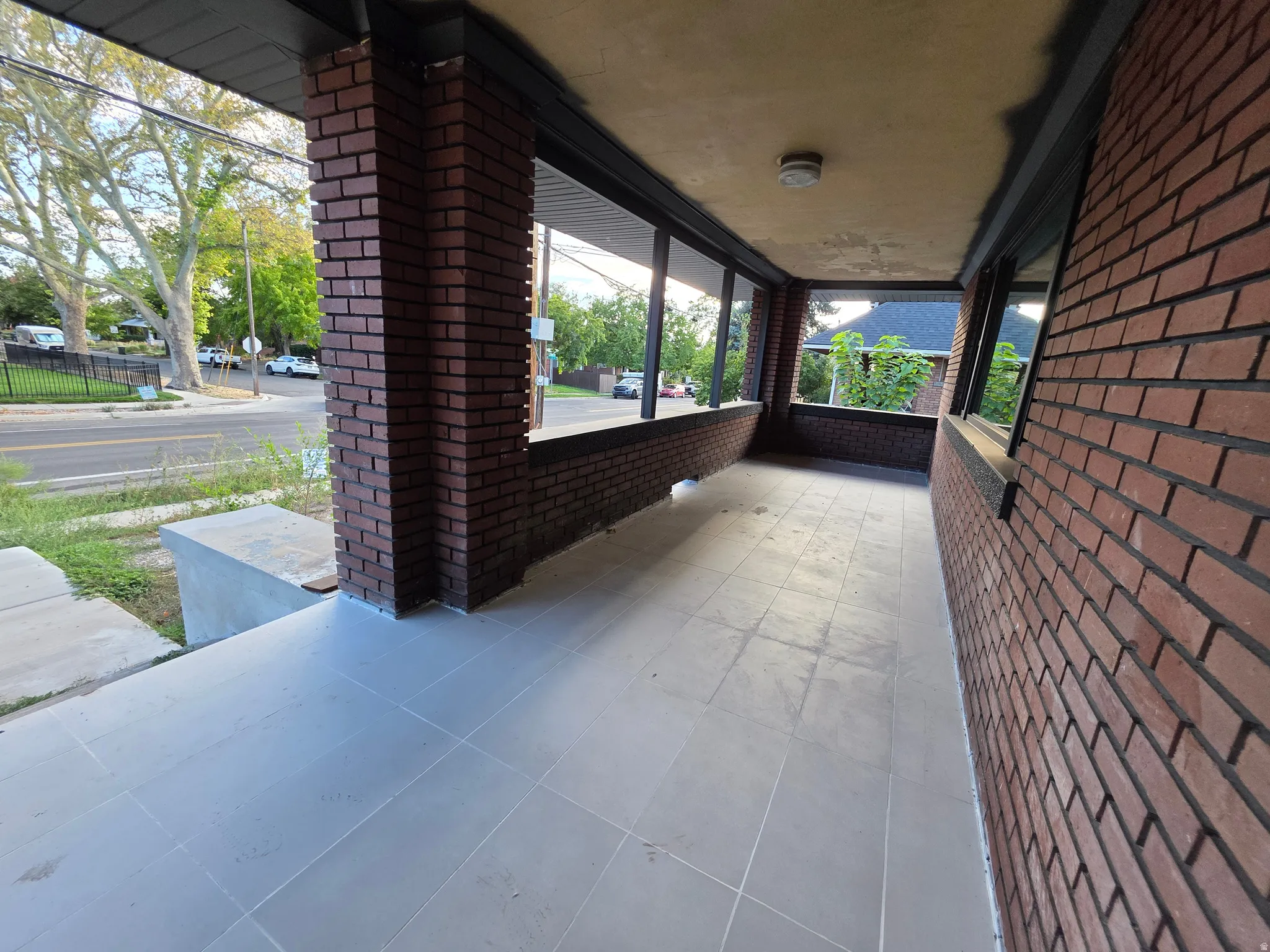 Expansive brick-clad porch with tile flooring, featuring brick columns and a recessed ceiling with an attached light fixture