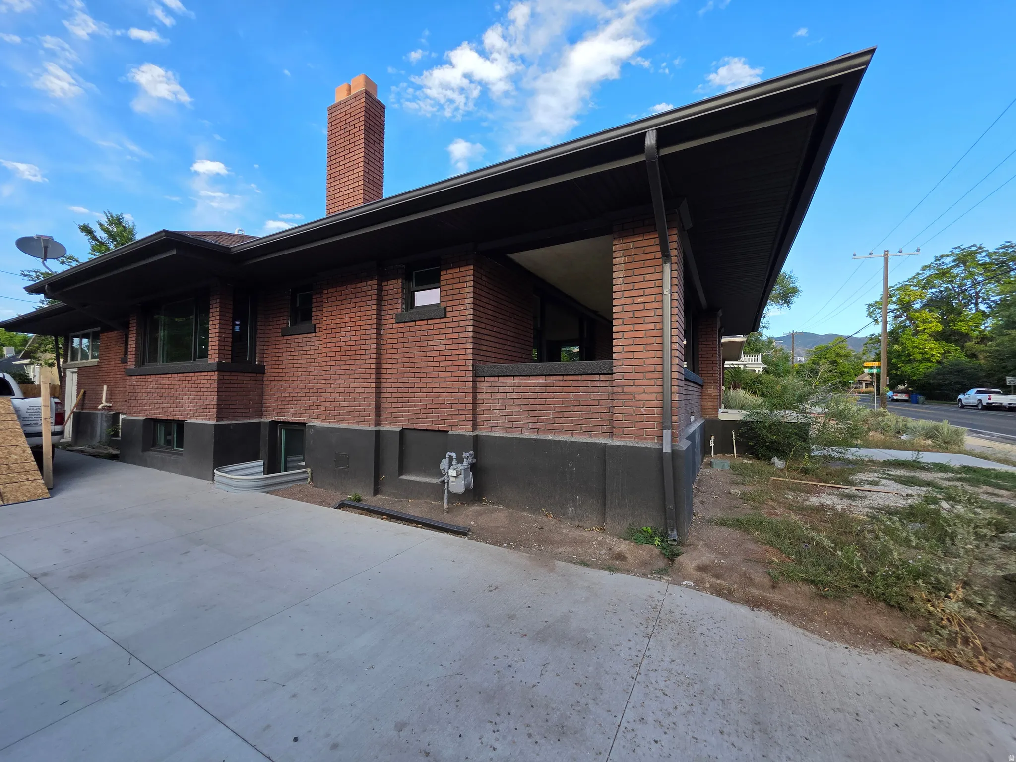Brick exterior with a prominent brick chimney, an expansive paved driveway, and multiple window wells