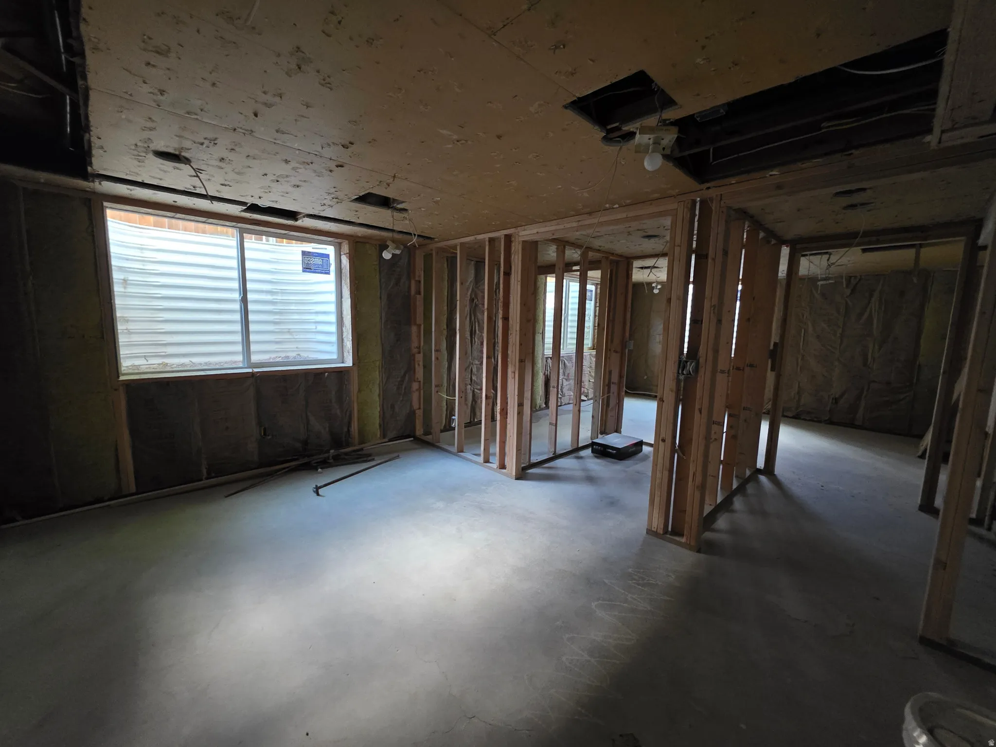 Unfinished lower level with wood framing, exposed ceiling joists, concrete flooring, and an egress window