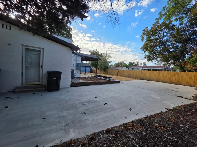 Expansive concrete patio, wooden privacy fence, mature trees, and a covered wooden deck