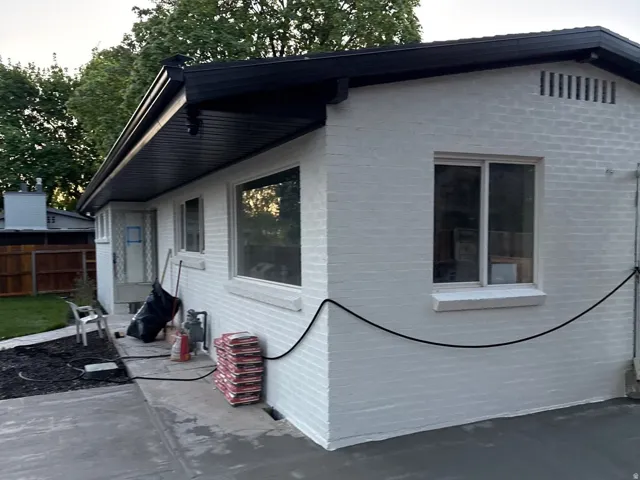 White brick exterior with a dark fascia, black gutters, and a newly paved concrete surface