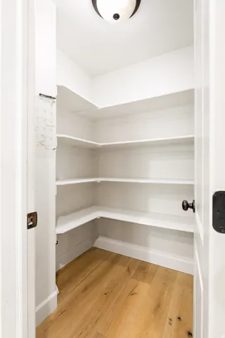 Spacious pantry featuring multiple tiers of built-in shelving, wood-finish flooring, and a flush mount light fixture
