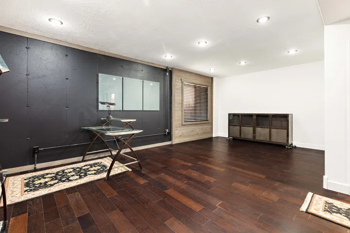 Dark wood-finish flooring, recessed ceiling lighting, a dark accent wall, and a textured wood-plank wall section