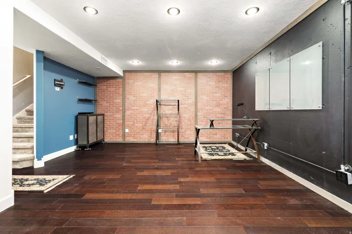 Hardwood-finish flooring, recessed lighting, exposed brick wall accents, industrial-style shelving, and a carpeted staircase