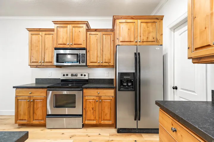 Wood cabinetry with crown molding, stainless steel appliances, dark stone-finish countertops, and wood-finish flooring