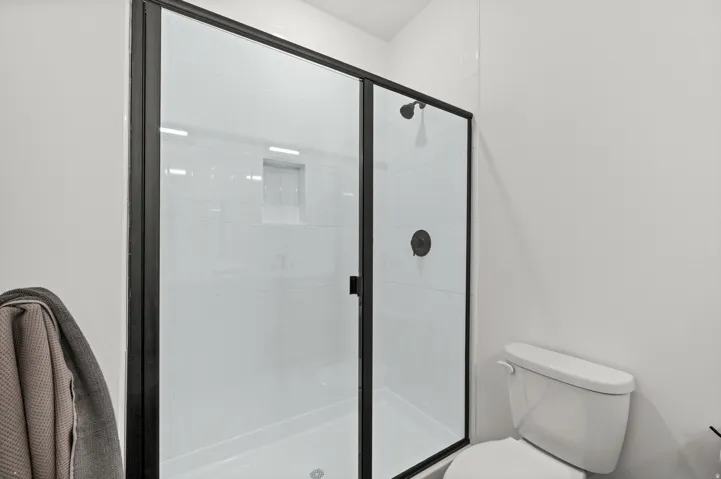 Walk-in shower with clear glass door, black frame, and a built-in shower niche