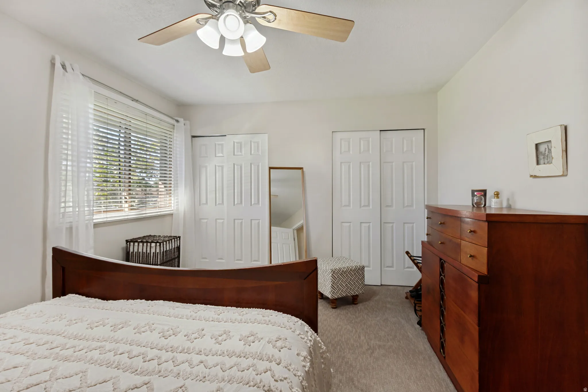 Recessed window with blinds and sheer curtains, ceiling fan with light fixture, light-toned carpeting, and bi-fold closet doors