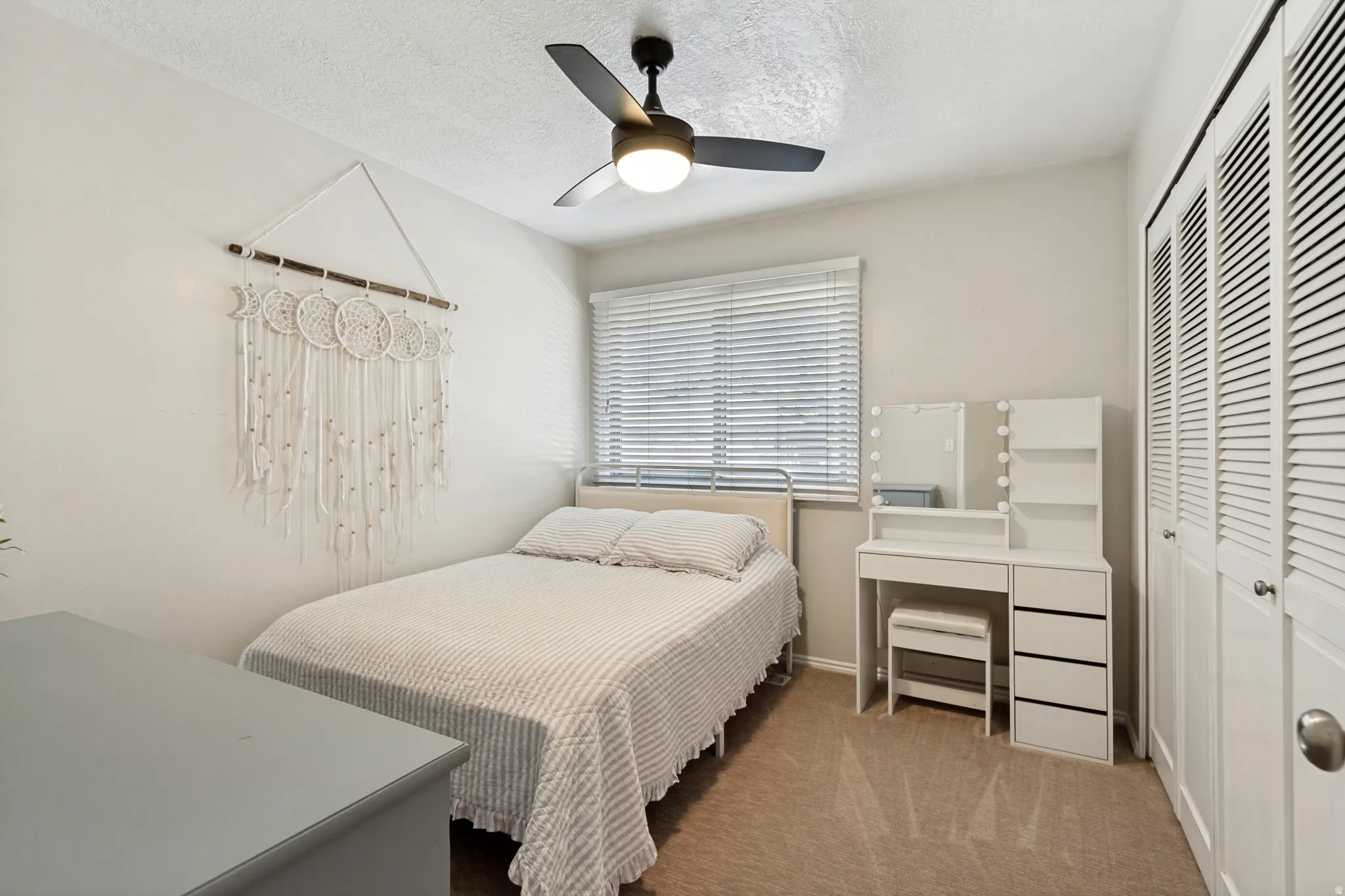 Neutral wall paint, ceiling fan with integrated lighting, window with horizontal blinds, and carpeted flooring