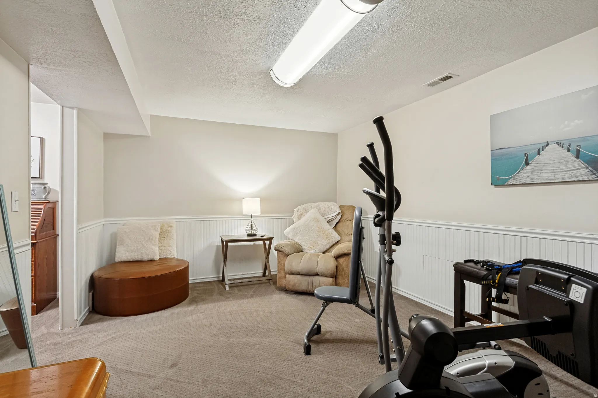 Recessed ceiling with an overhead fluorescent light fixture, carpeted flooring, and white wainscoting