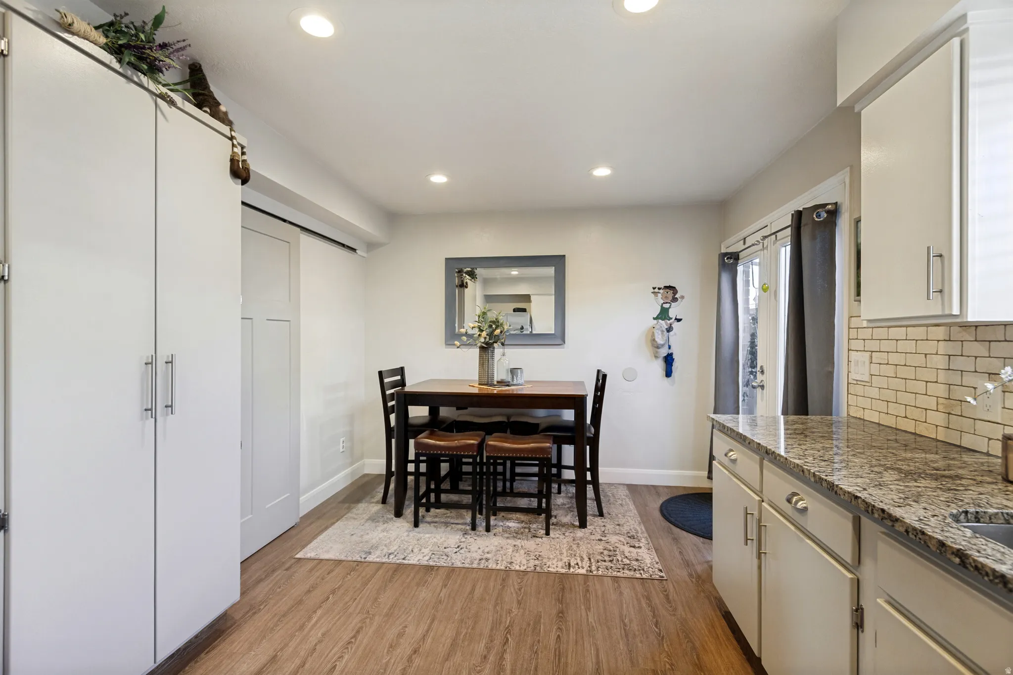 Recessed lighting illuminates the wood-finish flooring, kitchen cabinetry with granite countertops, and subway tile backsplash