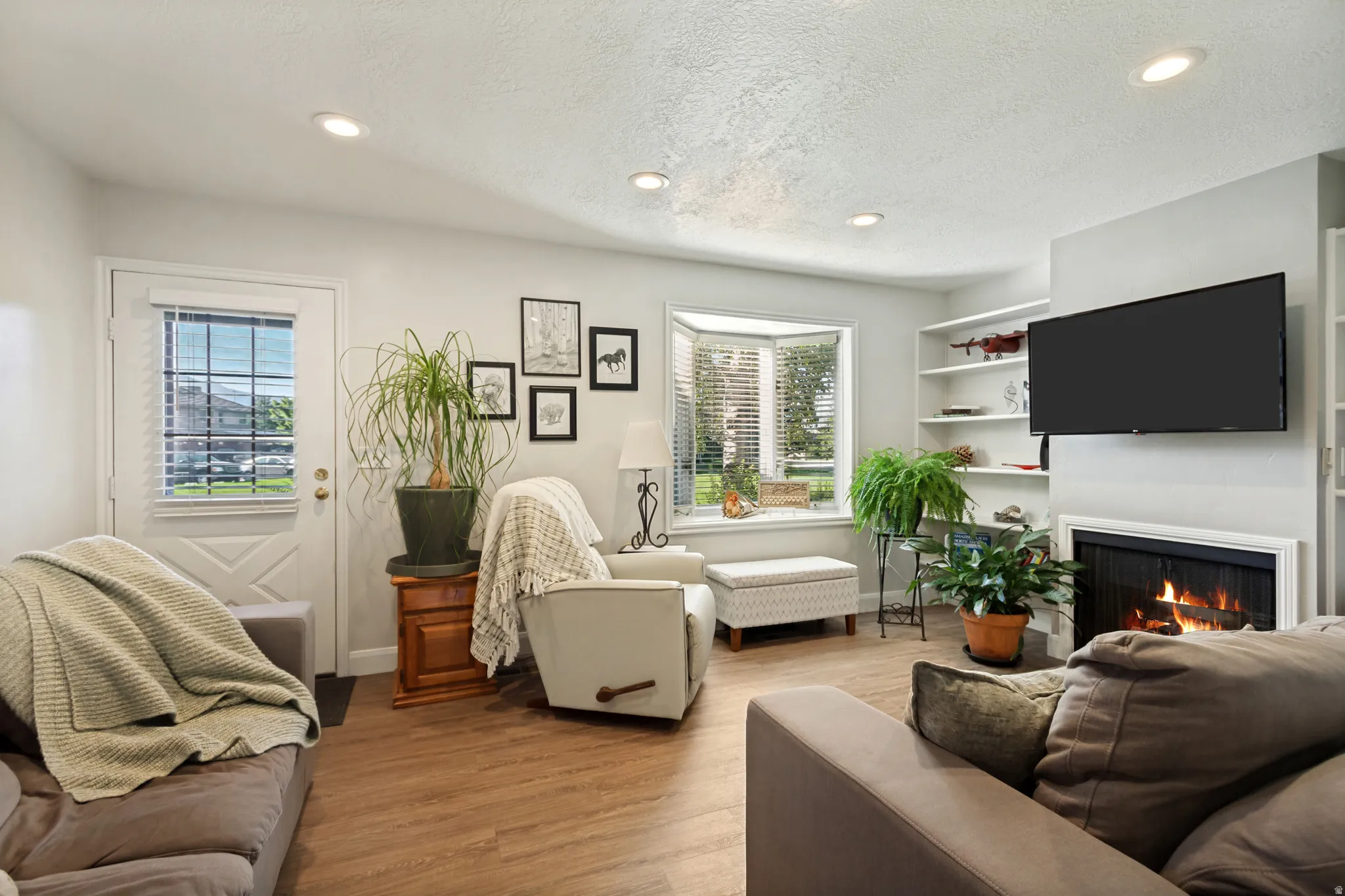 Wood-finish flooring throughout, recessed lighting, fireplace with a white mantel, built-in shelving, and a bay window