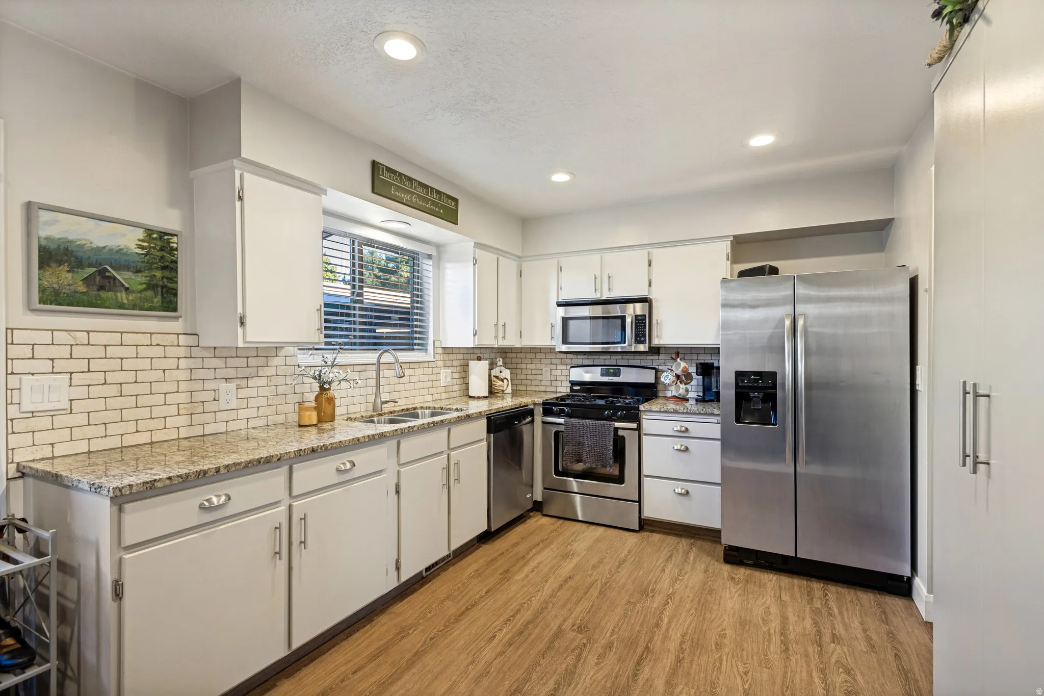 Kitchen featuring wood-finish flooring, white cabinetry, a subway tile backsplash, and stainless steel appliances