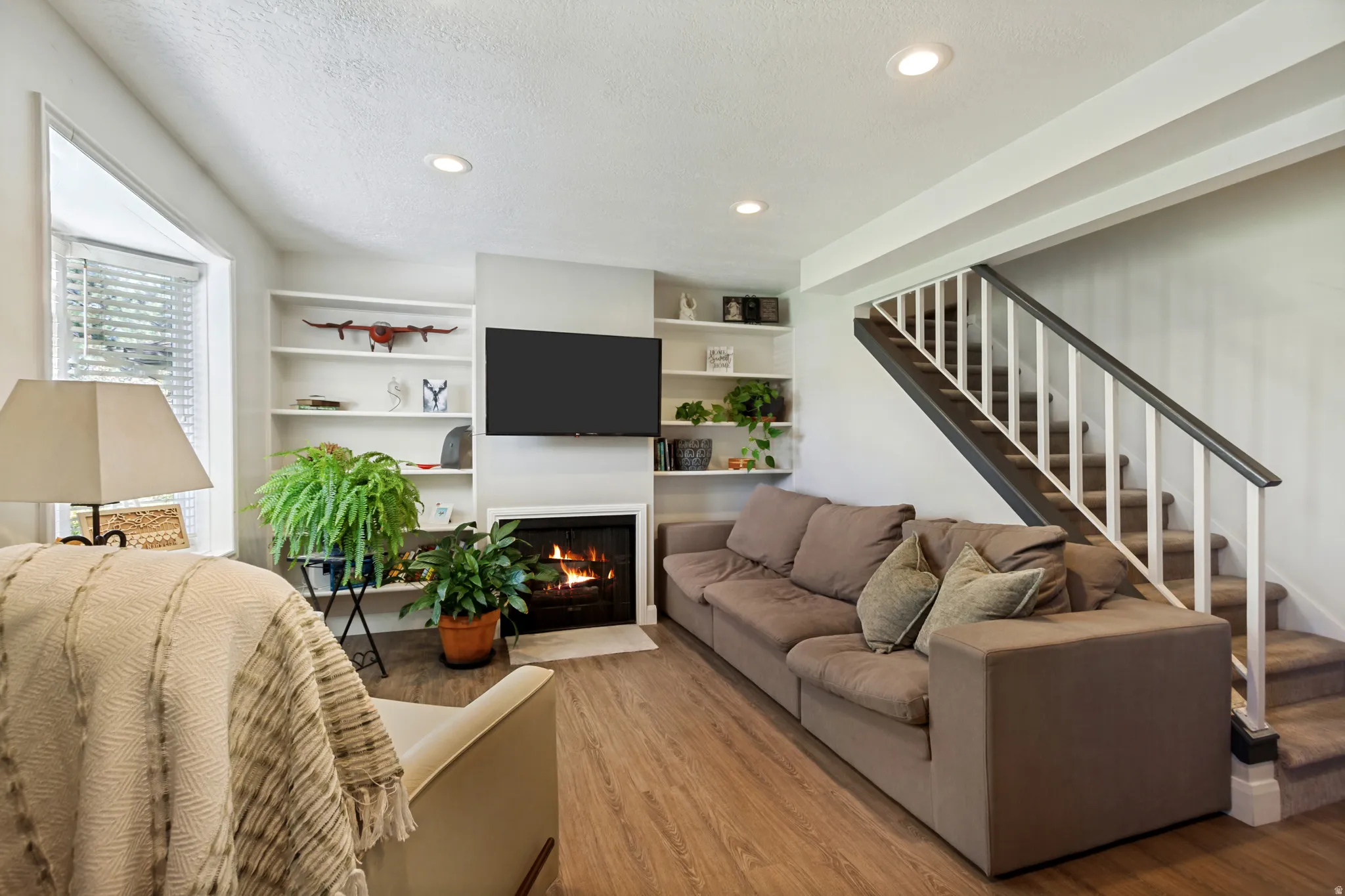 Living area featuring wood-finish flooring, a fireplace, recessed lighting, built-in shelving, and a carpeted staircase