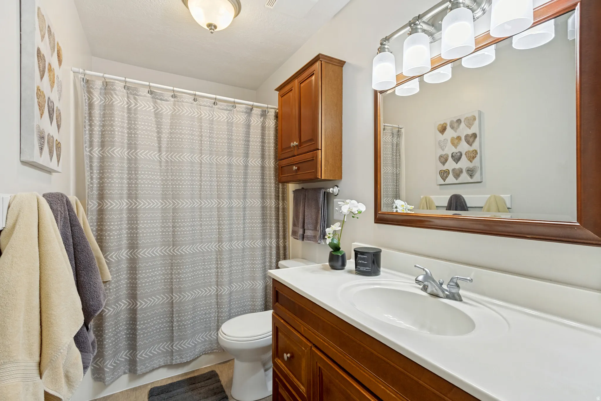 Bathroom featuring a vanity with a white countertop and wood-finish cabinetry, a framed mirror, and a wall-mounted light fixture with multiple sconces